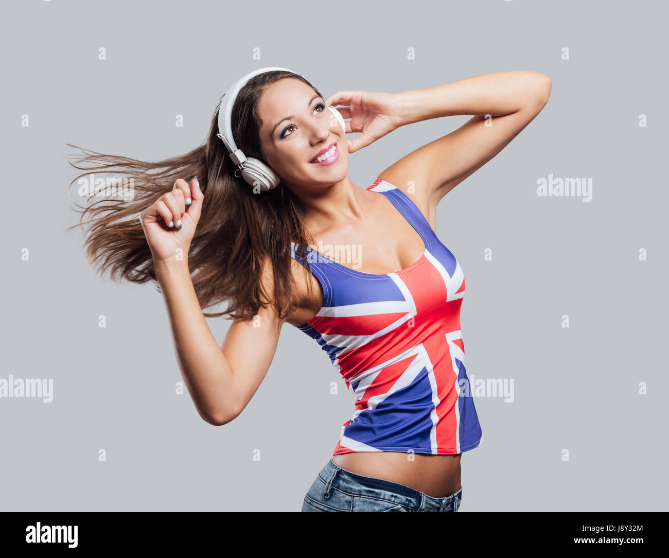 Sorridente ragazza adolescente indossando una bandiera inglese tank top,  ella è l'ascolto di musica con cuffie e ballo Foto stock - Alamy