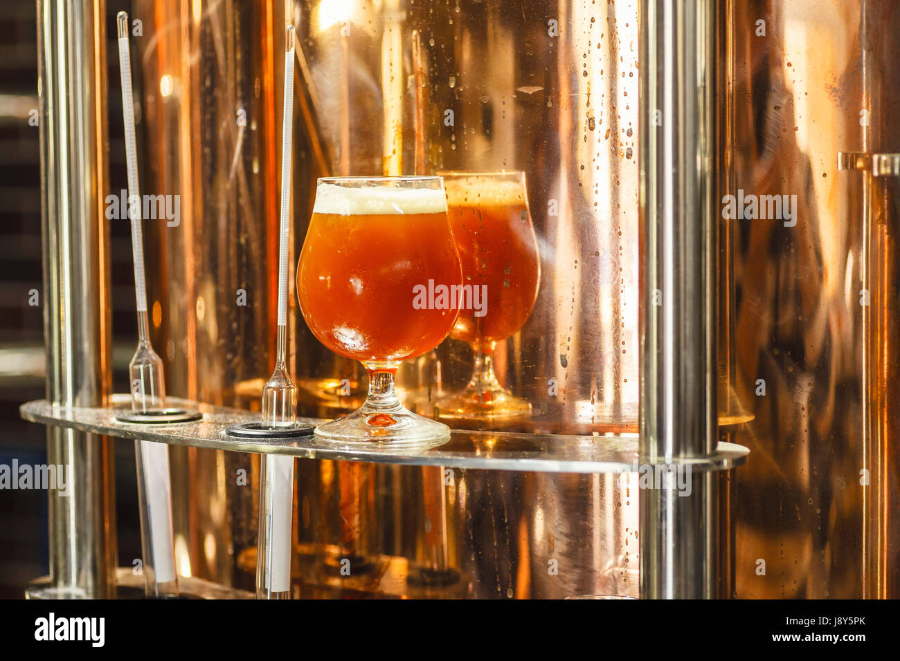 Bicchiere pieno di ale ambrata birra stare vicino a un lavoro bollitore di rame in una birreria commerciale con alcuni strumenti di misurazione Foto Stock