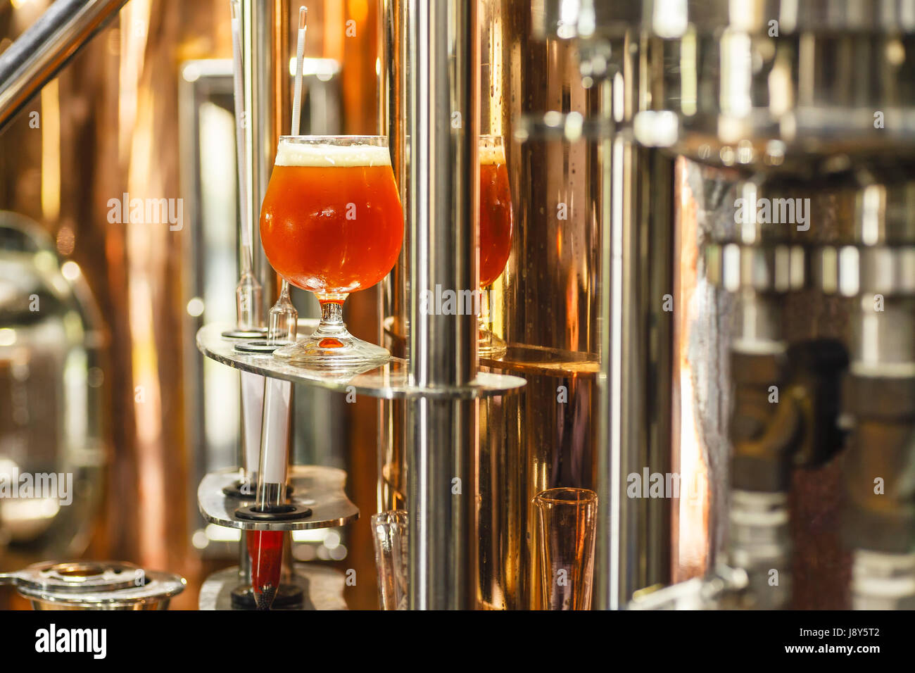 Bicchiere pieno di ale ambrata birra stare vicino a un lavoro bollitore di rame in una birreria commerciale con alcuni strumenti di misurazione Foto Stock