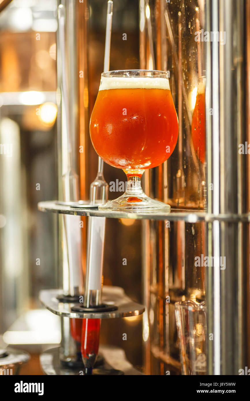 Bicchiere pieno di ale ambrata birra stare vicino a un lavoro bollitore di rame in una birreria commerciale con alcuni strumenti di misurazione Foto Stock