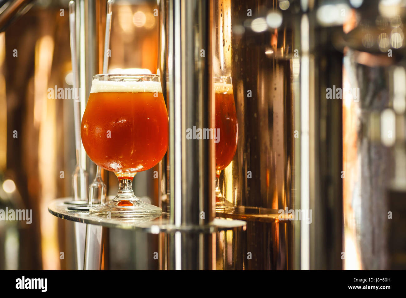 Bicchiere pieno di ale ambrata birra stare vicino a un lavoro bollitore di rame in una birreria commerciale con alcuni strumenti di misurazione Foto Stock