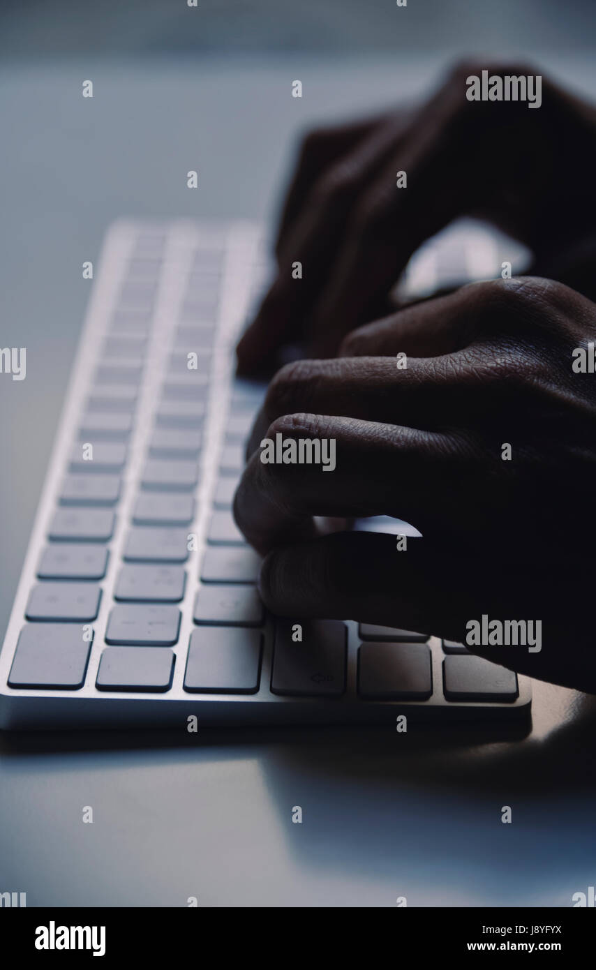Primo piano di un giovane uomo di digitazione in una tastiera di computer nell'oscurità, con un effetto drammatico Foto Stock