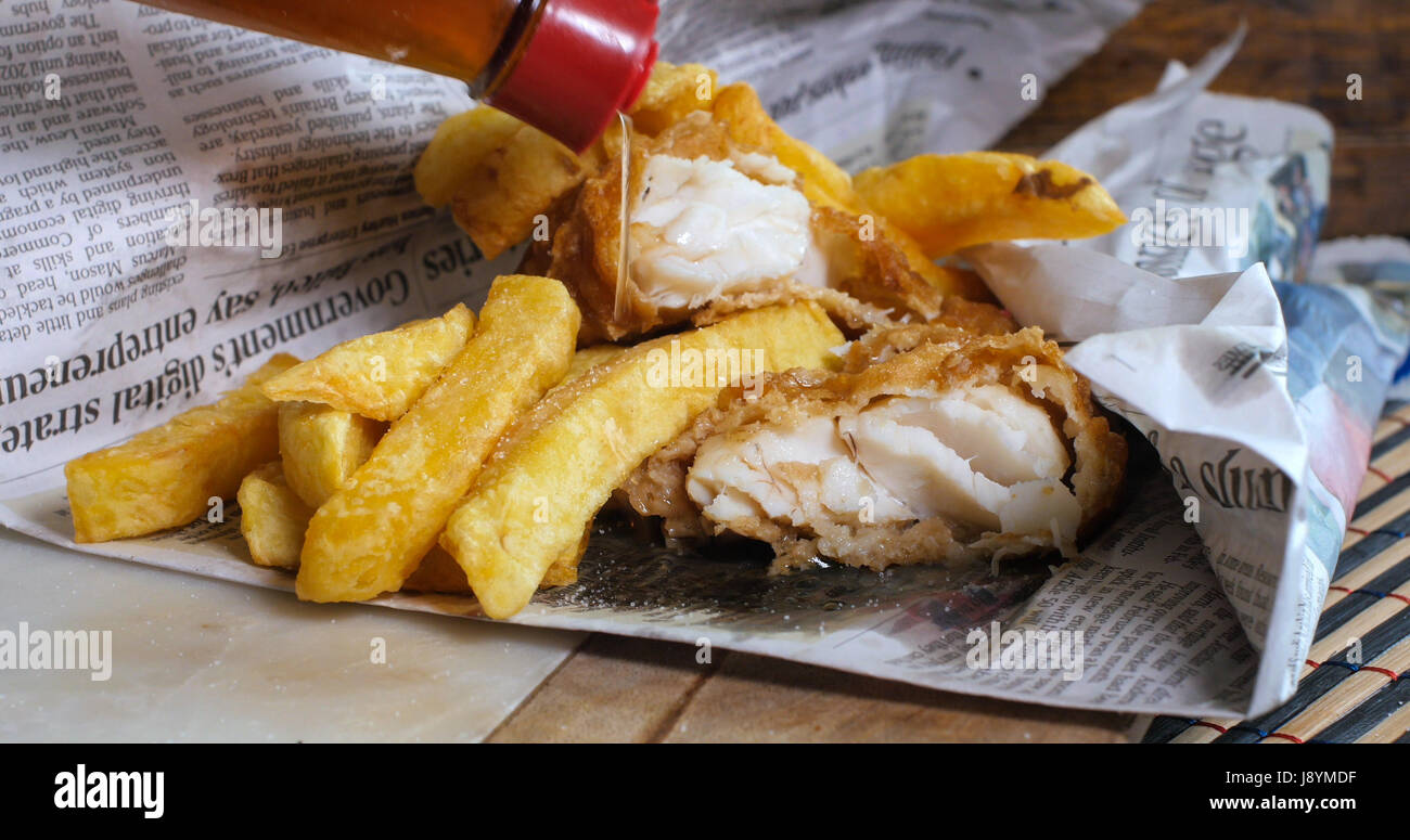 Aggiunta di aceto in un inglese di pesce e patatine avvolti in un giornale, il modo tradizionale Foto Stock