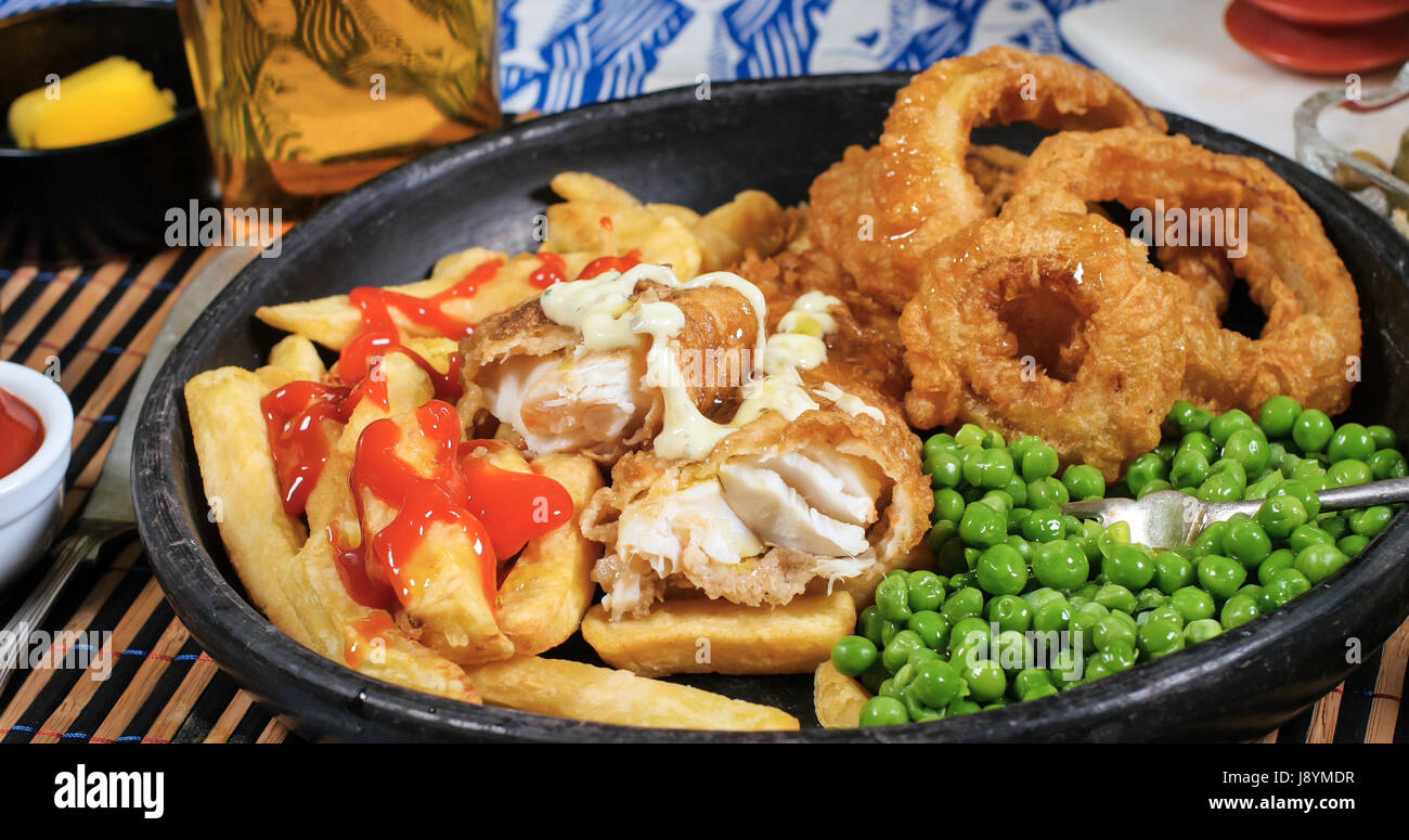 Vista di un inglese di pesce e patatine fritte con giardino piselli, anello cipolle e salsa tartara Foto Stock