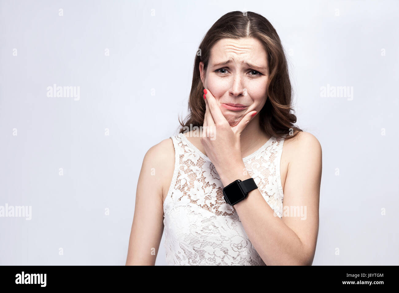 Ritratto di donna bella con le lentiggini e abito bianco e smart guarda con dente dolore su argento grigio. Salute e medicina concetto. Foto Stock