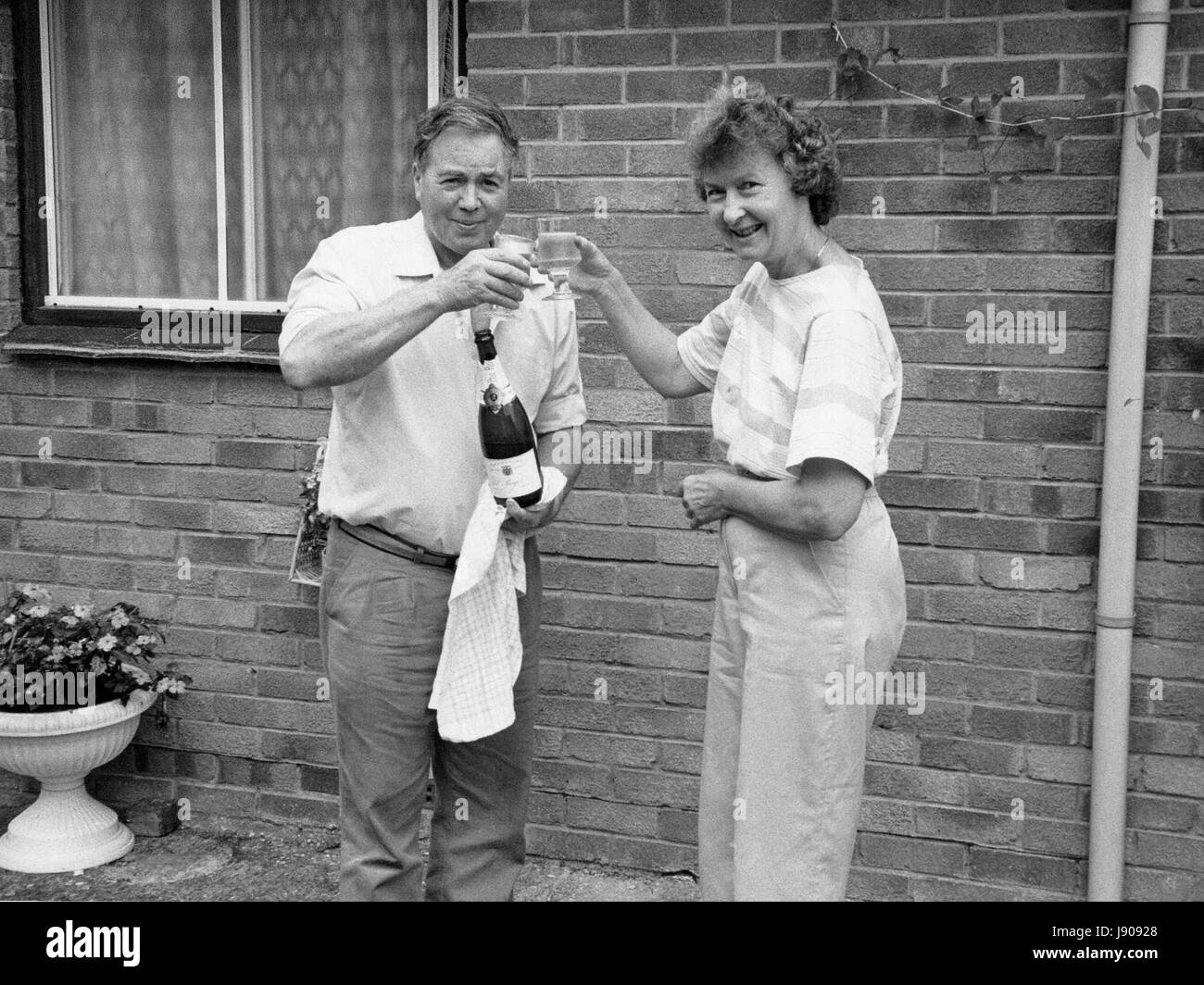 Una coppia di coniugi nei loro primi anni sessanta festeggiare il pensionamento con un bicchiere di vino frizzante al di fuori della loro casa nei pressi di segale, Inghilterra circa 1987. Foto Stock