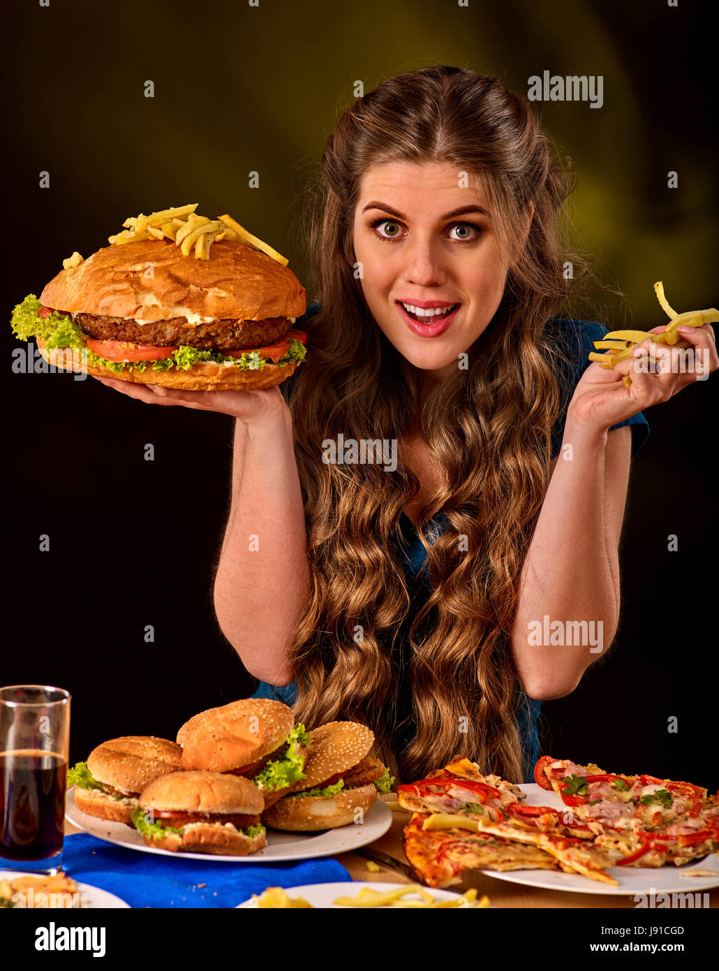 Donna di mangiare patatine e hamburger sul tavolo. Foto Stock