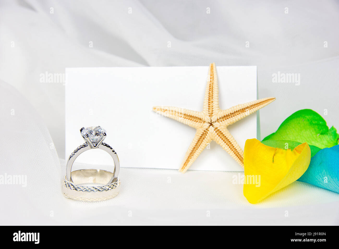 Gli anelli di nozze e starfish su tulle con colorati petali di rosa e bianco vuoto posto card Foto Stock