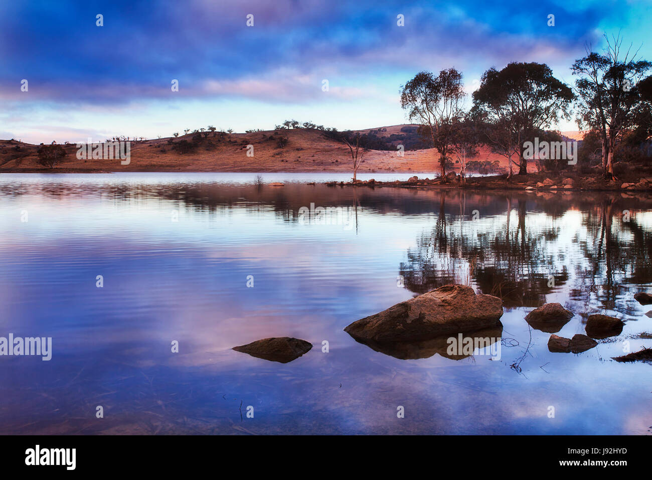 BLue sunrise oltre la collina di gamma e ancora acque di acqua dolce lago Jindabyne nelle montagne innevate regione del NSW, Australia. Gomma-alberi e boul eccezionale Foto Stock