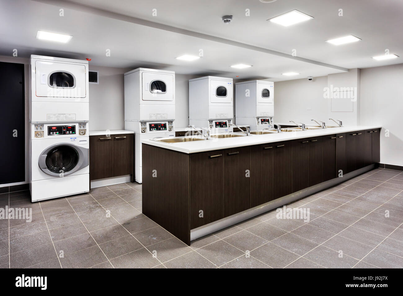 Potenti macchine lavanderia e Asciugatori automatici in grande lavanderia a gettoni con un armadio lavelli per risciacquo e acqua di rubinetto. Foto Stock