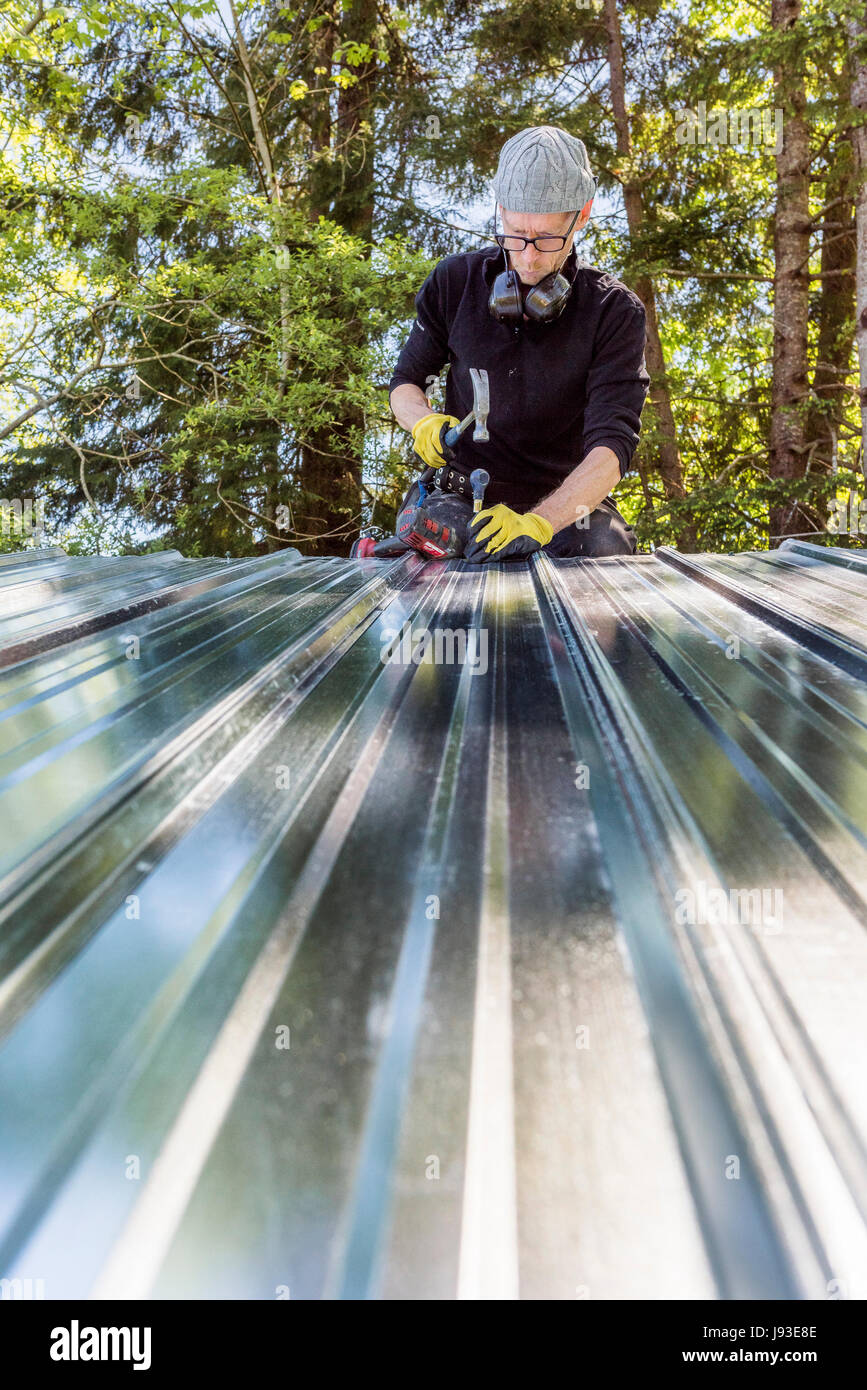 Uomo al lavoro installazione tetto metallico su capannone. Foto Stock