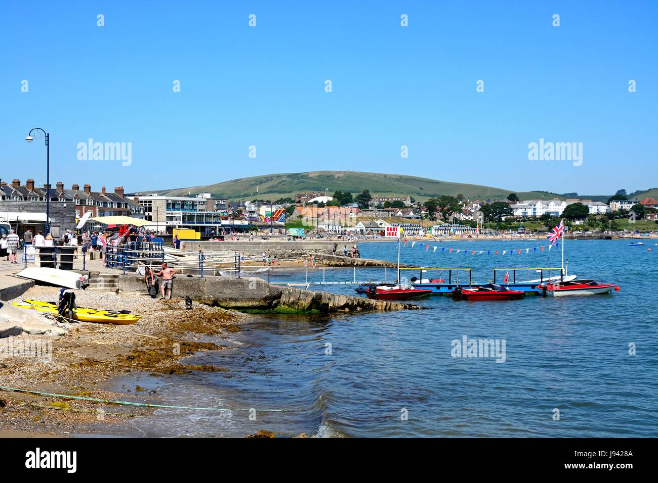 Barche ormeggiate lungo un piccolo molo con vista lungo la spiaggia con la città verso la parte posteriore, Swanage Dorset, Inghilterra, Regno Unito, Europa occidentale. Foto Stock