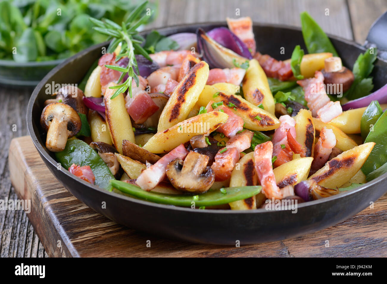 Bavarese dito fritto a forma di gnocchi di patate con verdure e pancetta affumicata, la valeriana come insalata di contorno Foto Stock