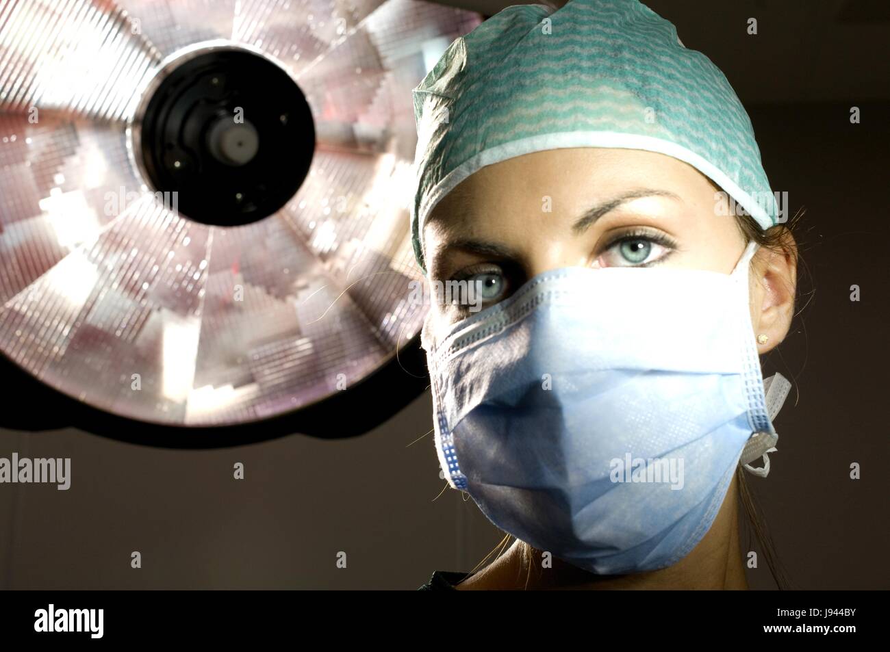 Chirurgo in sala operatoria con mascherina chirurgica e chirurgica prepara il cappuccio donna femmina del paziente Foto Stock