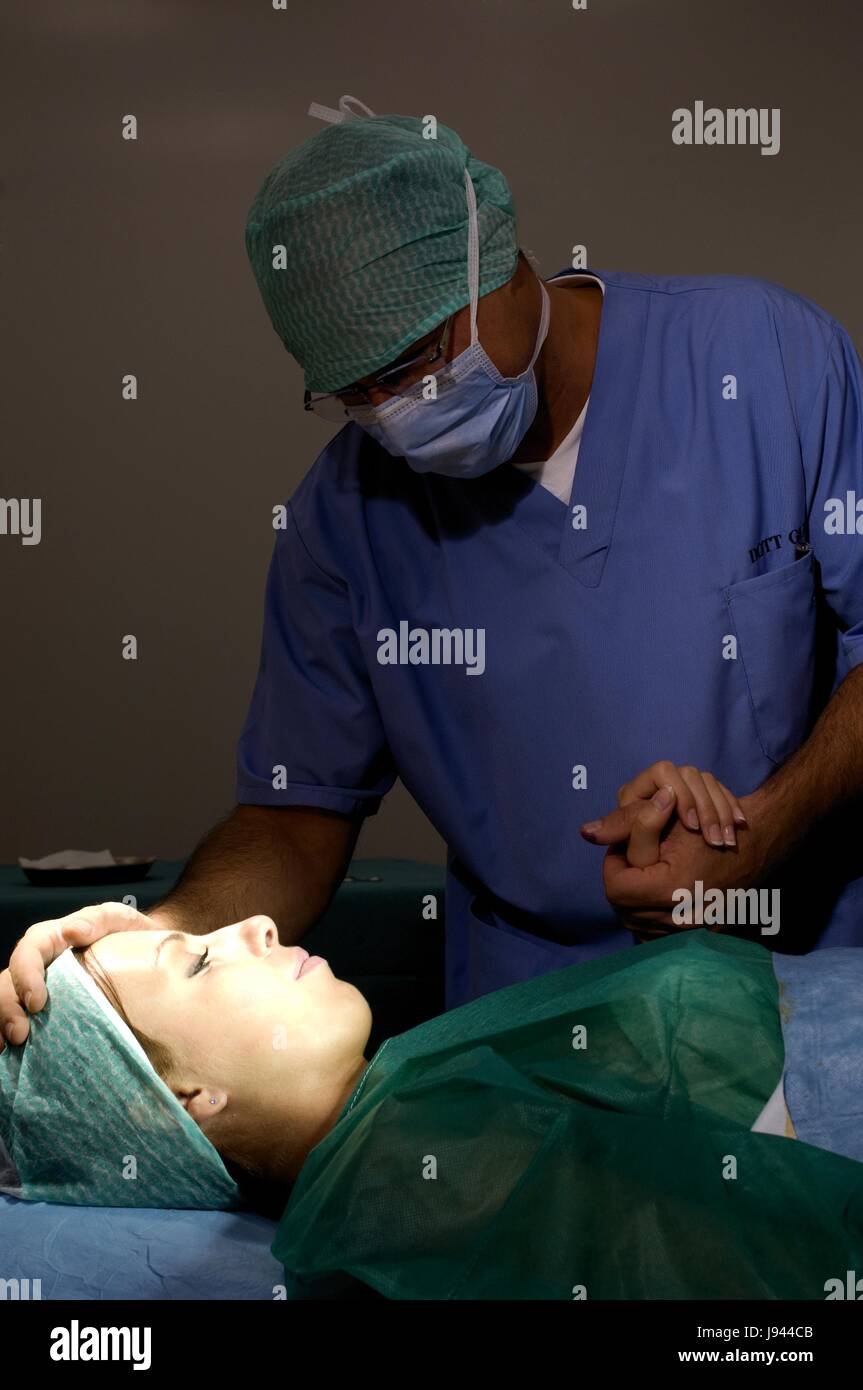Chirurgo in sala operatoria con mascherina chirurgica e chirurgica prepara il cappuccio donna femmina del paziente Foto Stock