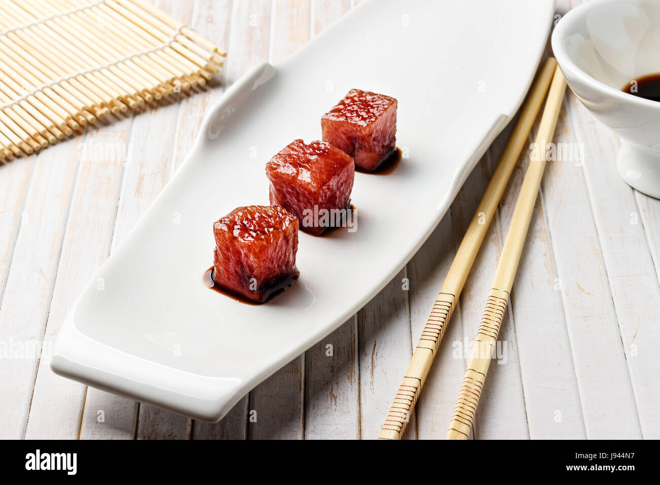 Tonno sashimi immerso in salsa di soia con bacchette di bambù e mat. Pesce crudo in tradizionale stile Giapponese. L'immagine orizzontale. Foto Stock