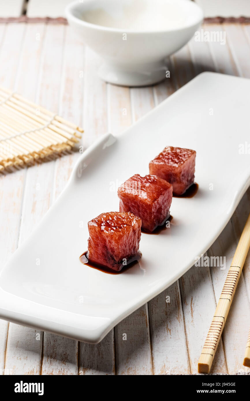Tonno sashimi immerso in salsa di soia con bacchette di bambù e mat. Pesce crudo in tradizionale stile Giapponese. L'immagine verticale. Foto Stock