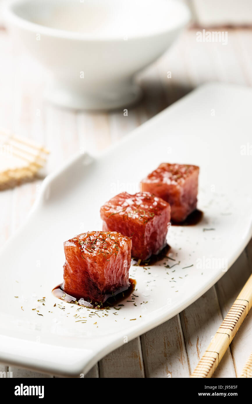 Tonno sashimi immerso in salsa di soia, spessa sale e aneto con bacchette di bambù e mat. Pesce crudo in tradizionale stile Giapponese. L'immagine verticale. Foto Stock