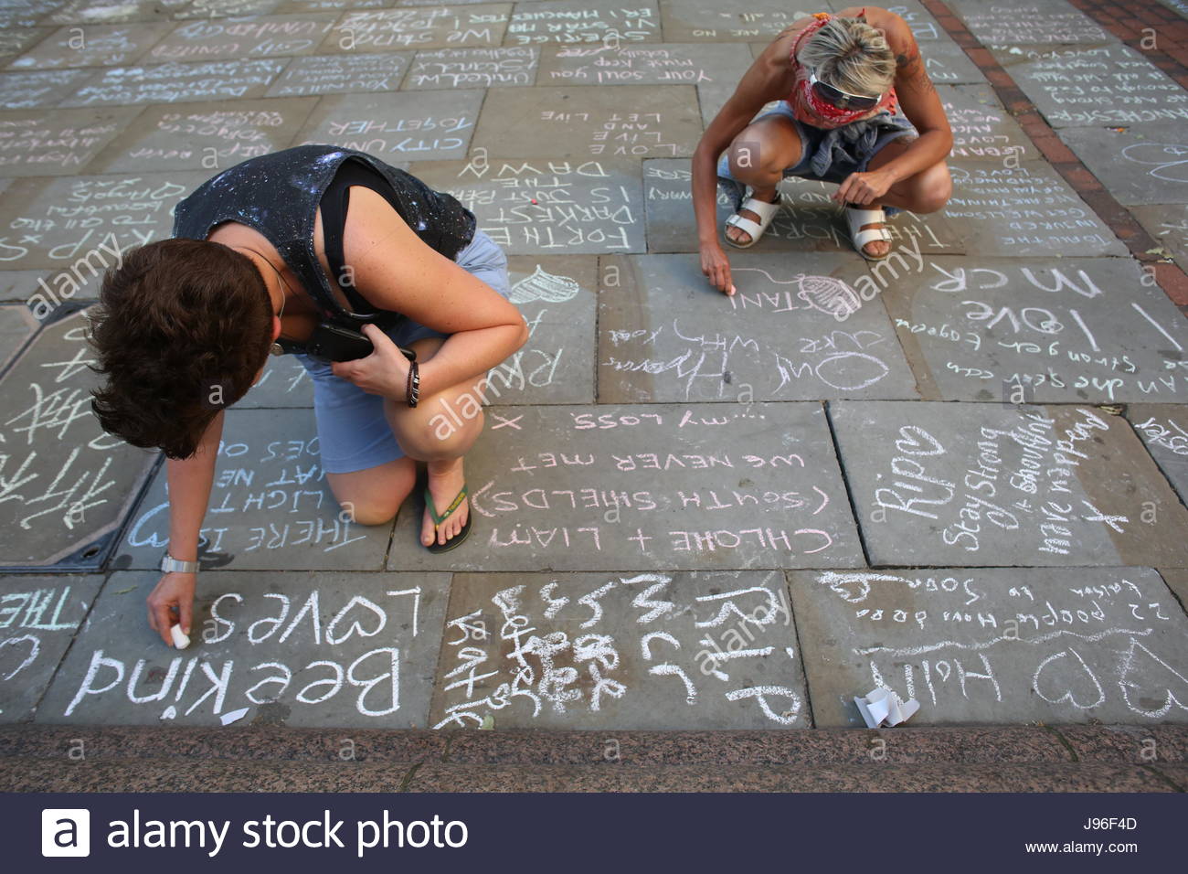 Due donne di ritegno messaggi di sostegno e di cordoglio sulla strada per le vittime dei bombardamenti di Manchester in St Ann's Square Foto Stock