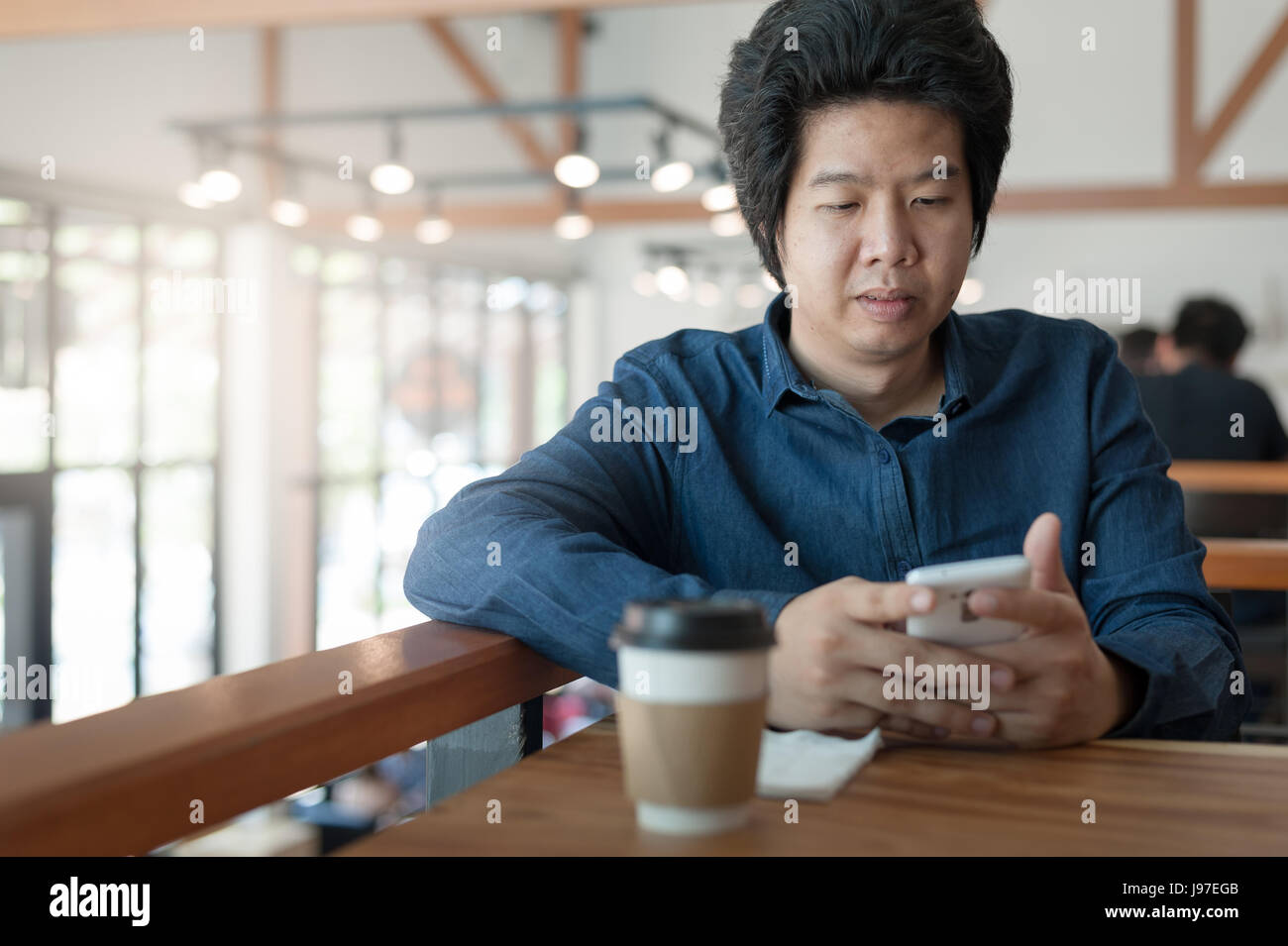 Adulto asiatici imprenditore freelance utilizza lo smartphone per la rete sociale mentre è seduto nella caffetteria sul weekend. Lo stile di vita di relax con caffè Foto Stock