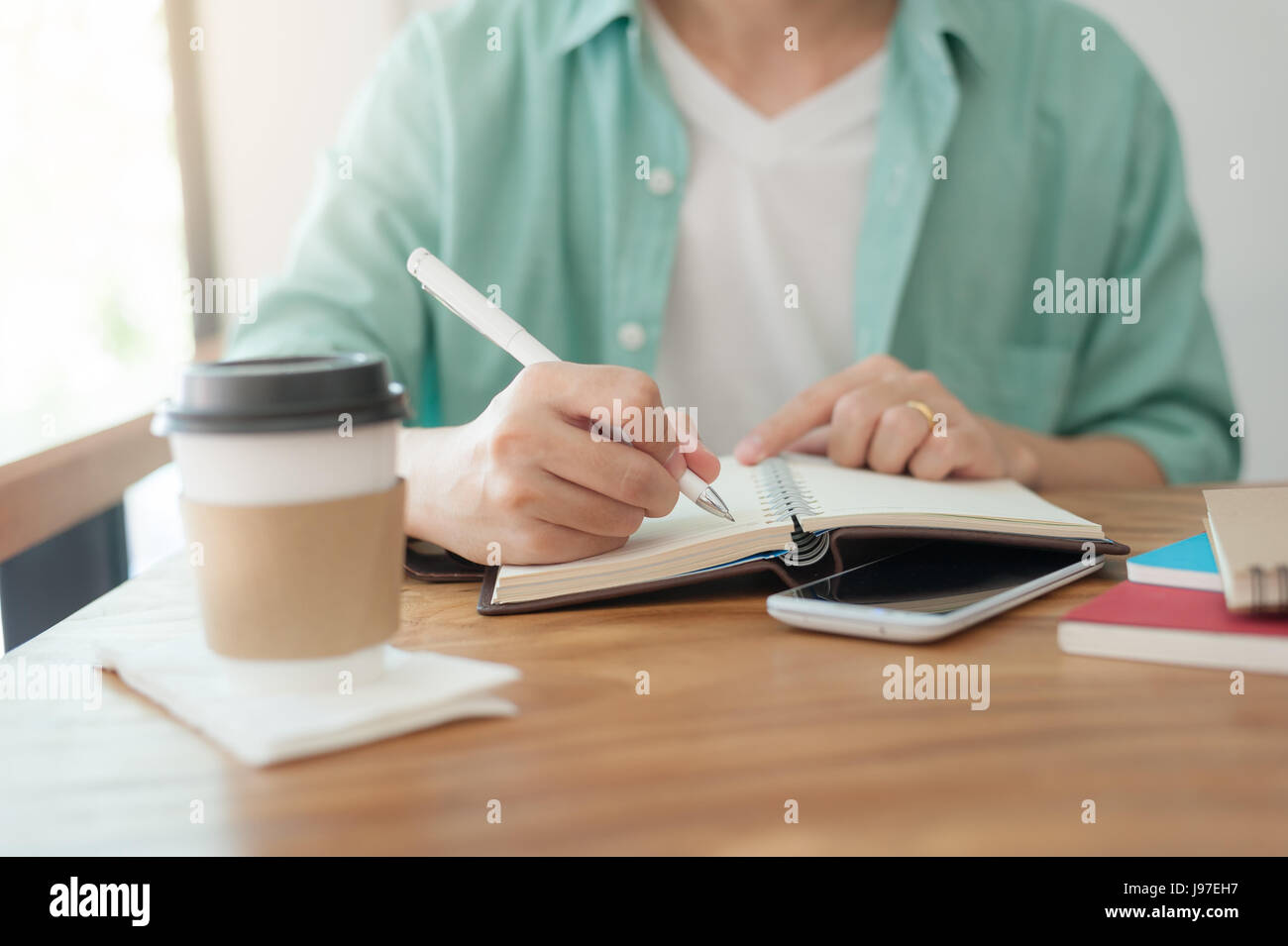 Asian freelancer con panni informale scritta sul notebook in coffee shop. Esternalizzare il lavoratore allo stile di vita e attività sulla giornata lavorativa Foto Stock