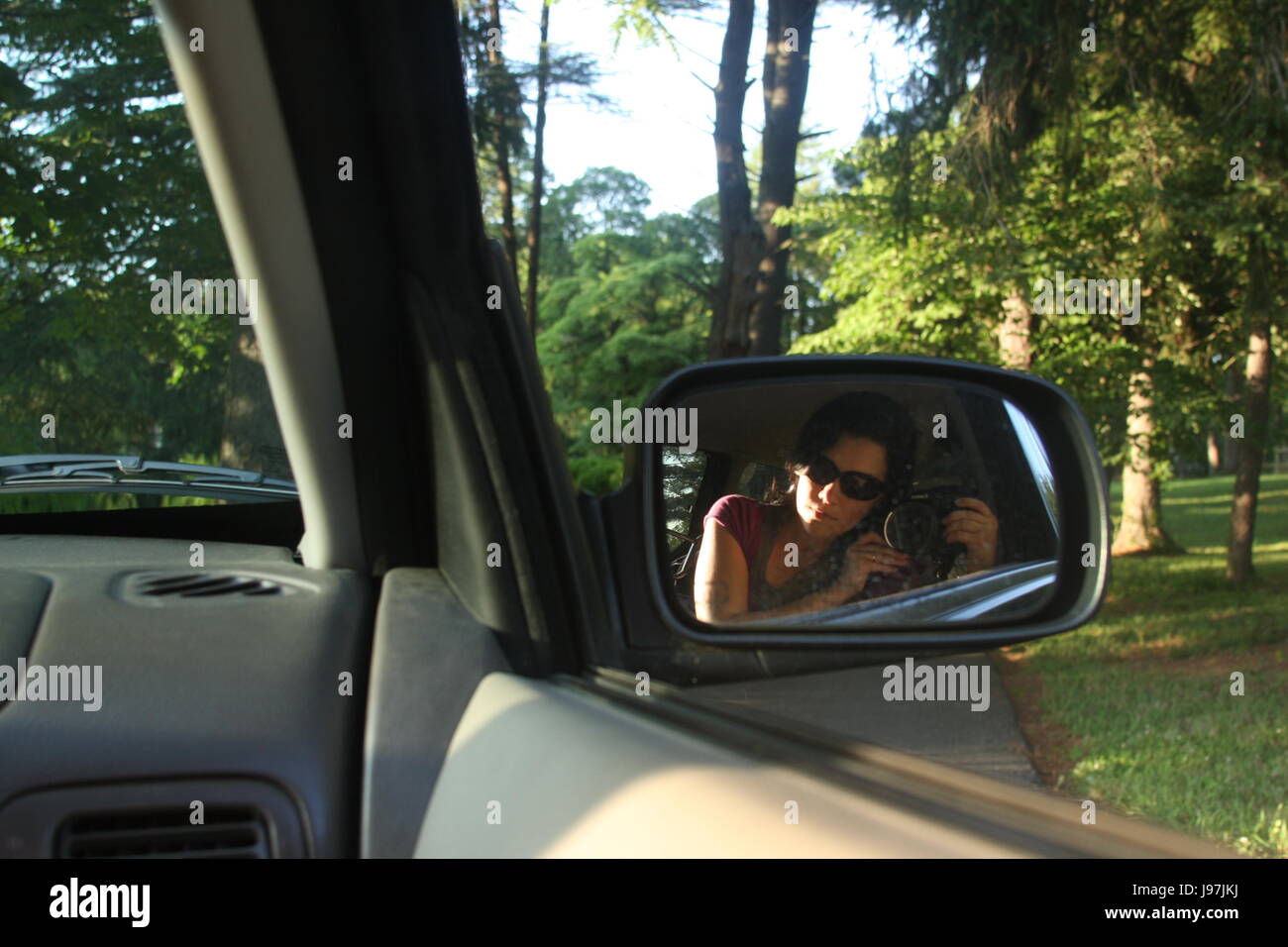 Giovane donna prendendo immagine di se stessa attraverso auto del finestrino laterale Foto Stock