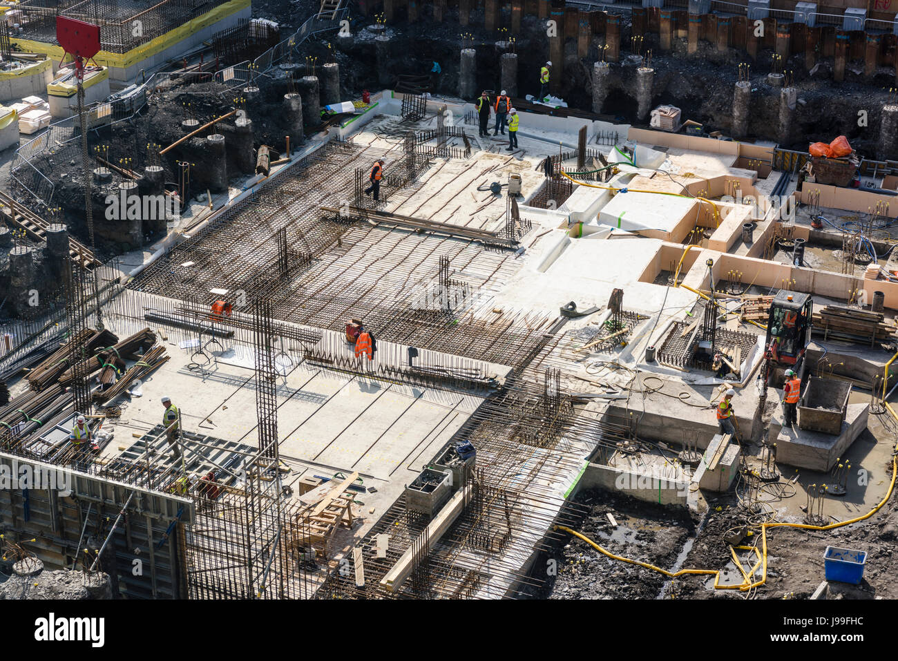 Lavoratori edili versare cemento in forma il lavoro per creare le basi di una a più piani di acciaio e cemento di edificio. Foto Stock