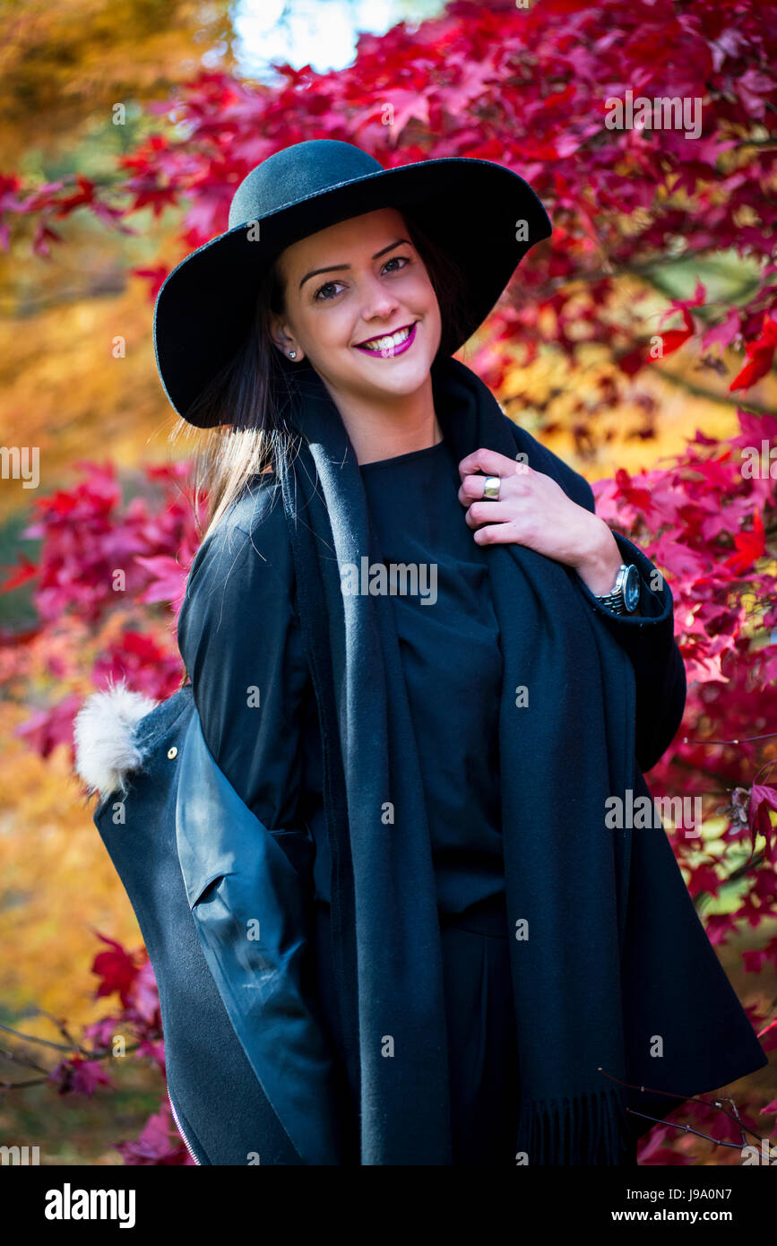 Signora giovane godendo di caldi colori autunnali nei boschi circondate da acero canadese lasciare gli alberi e il giapponese acer alberi di acero, sfumature di rosso, arancione Foto Stock