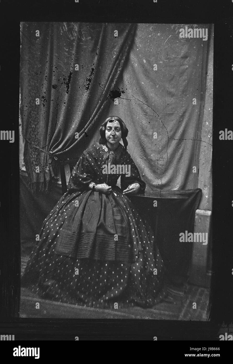 Portret van een onbekende jonge vrouw dieci voeten uit, zittend op stoel naast tafeltje (max res) Foto Stock