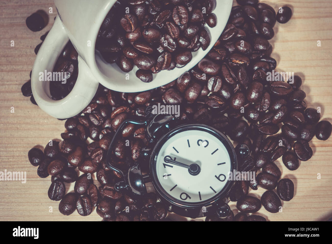 Orologio sveglia su i chicchi di caffè. Tazza da caffè piena di chicchi di caffè. Foto Stock