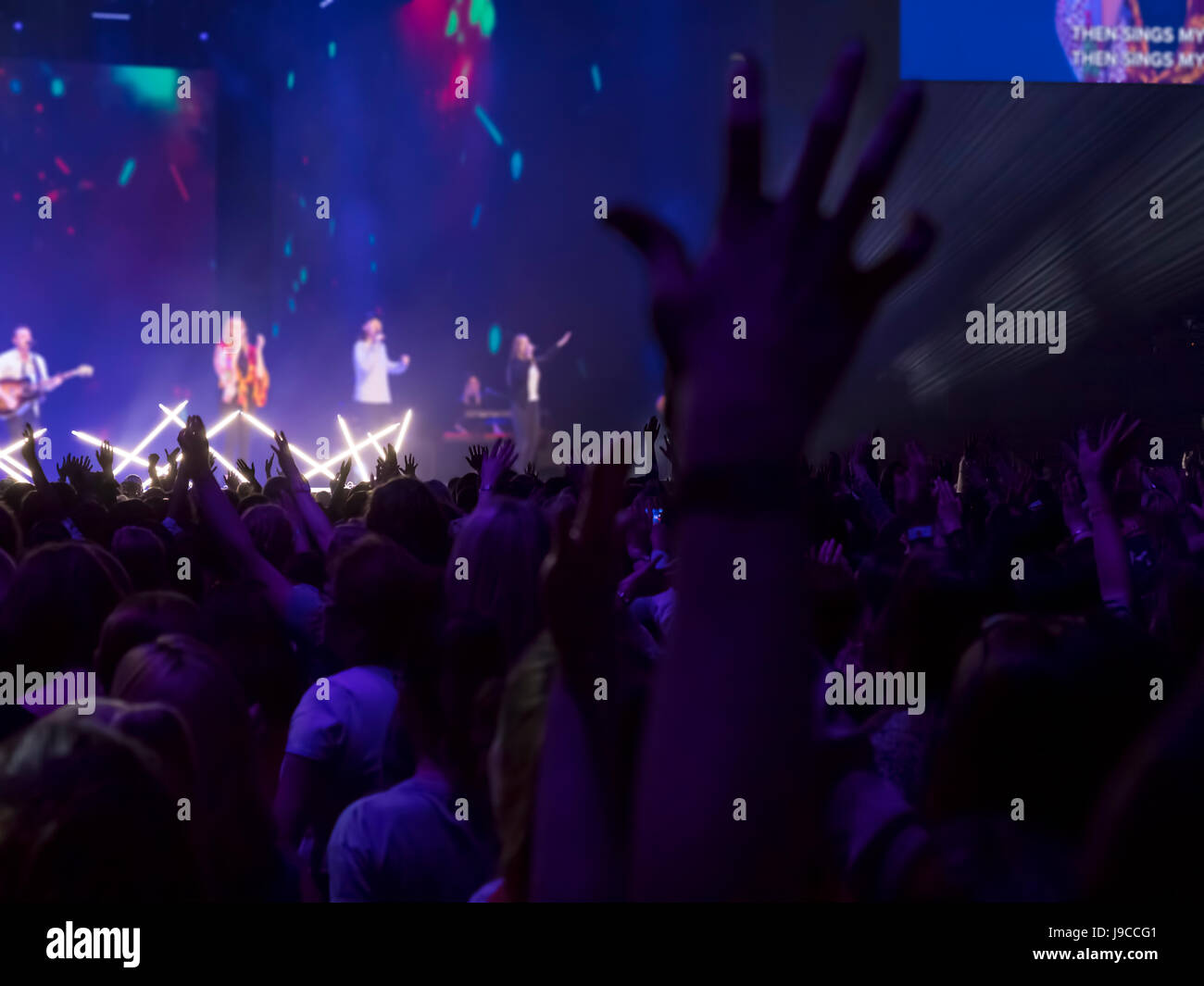 Udienza con le mani sollevate a un festival di musica e luci streaming verso il basso a partire da sopra il palcoscenico. Focus sulle mani Foto Stock