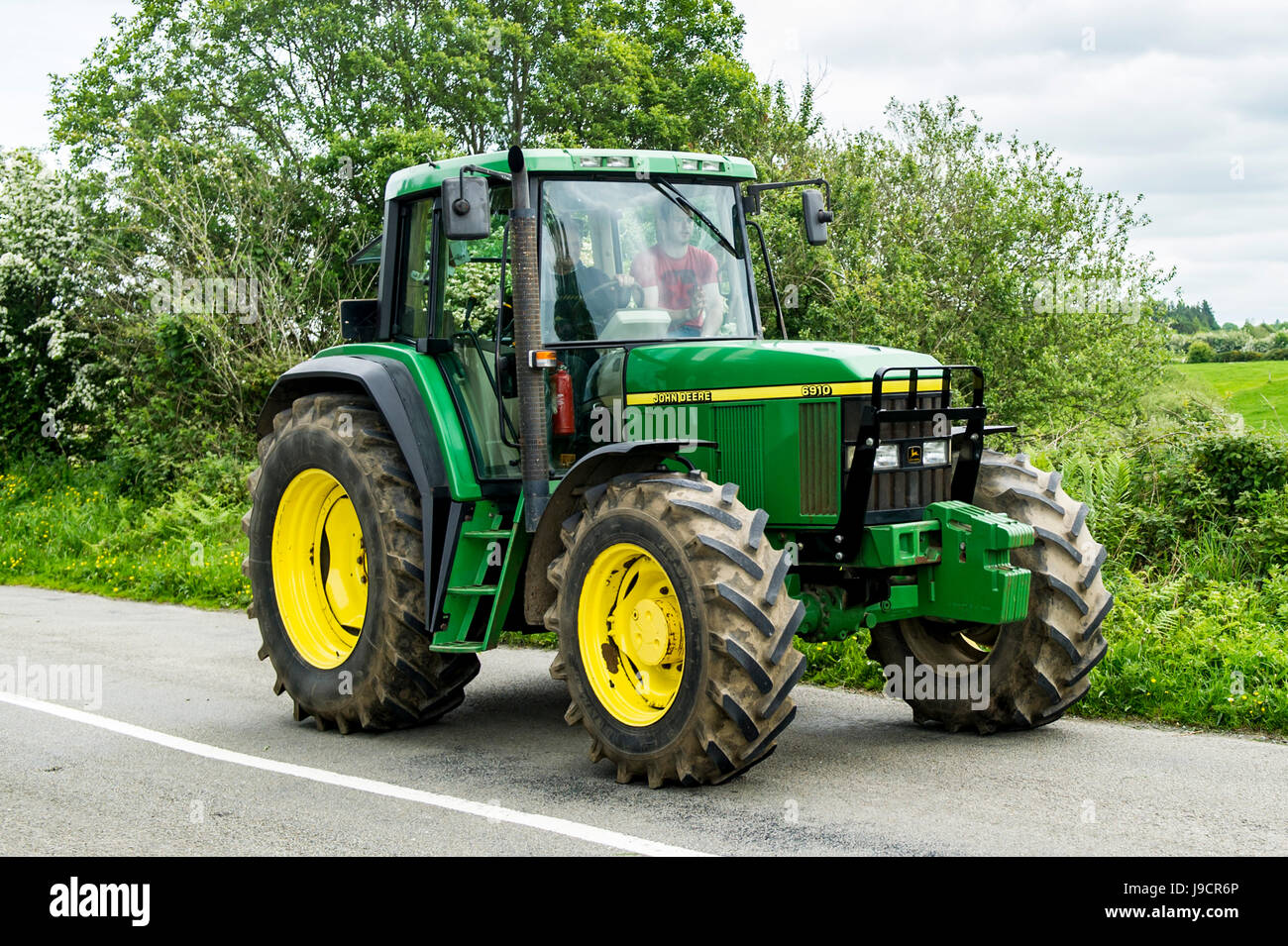 John Deere 6910 trattore viaggia lungo una strada di campagna in Irlanda con spazio di copia Foto Stock