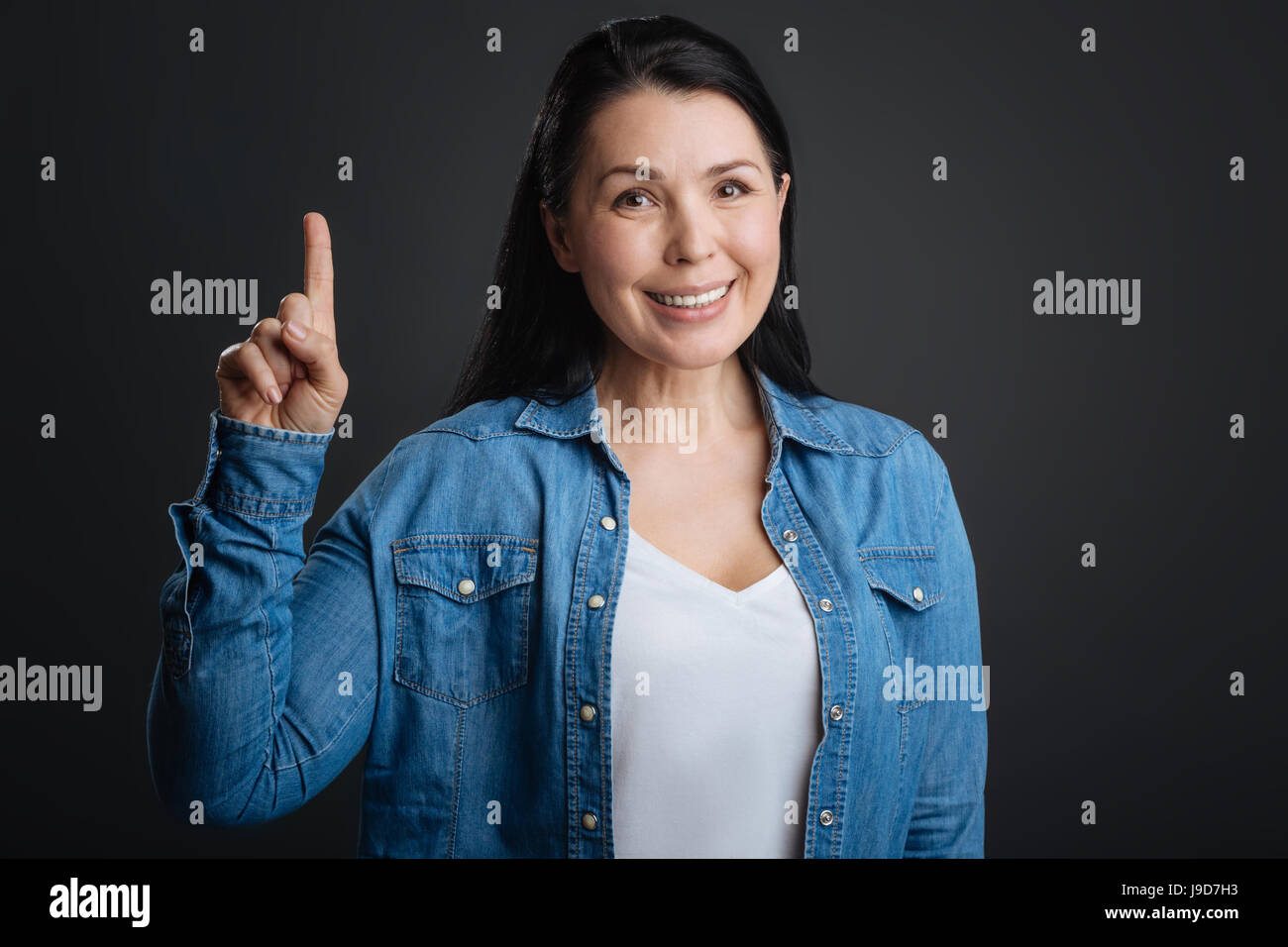 Prestare attenzione. Positivo gorgeous gentile signora usando un gesto a mano per il disegno di tutti attenzione mentre in piedi isolato su sfondo grigio Foto Stock