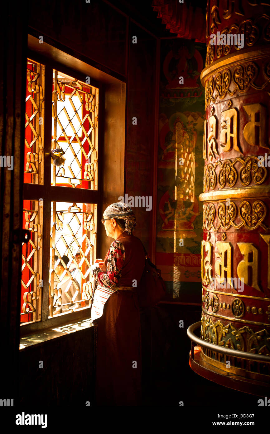 Una donna tibetana sorge accanto ad una grande ruota di preghiera del tempio di Boudhanath Stupa, Kathmandu, Nepal, Asia Foto Stock