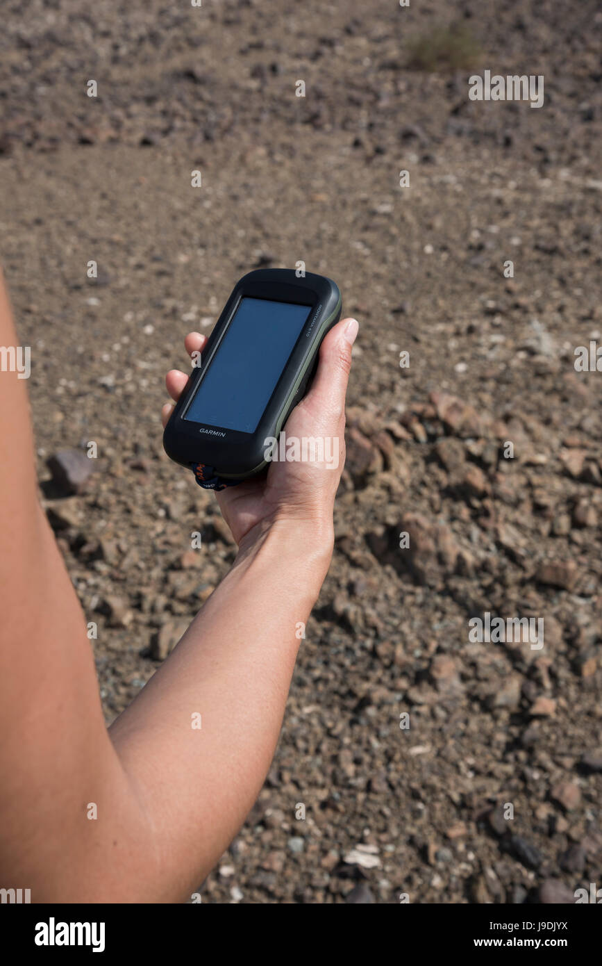 Una donna controlla un dispositivo GPS portatile mentre cammina su montagne aride, concentrandosi sulla navigazione in un paesaggio accidentato Foto Stock