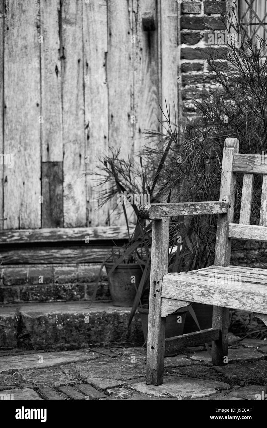Bella la quintessenza Inglese antico giardino di campagna immagine della sedia in legno accanto al vintage porta posteriore in bianco e nero Foto Stock