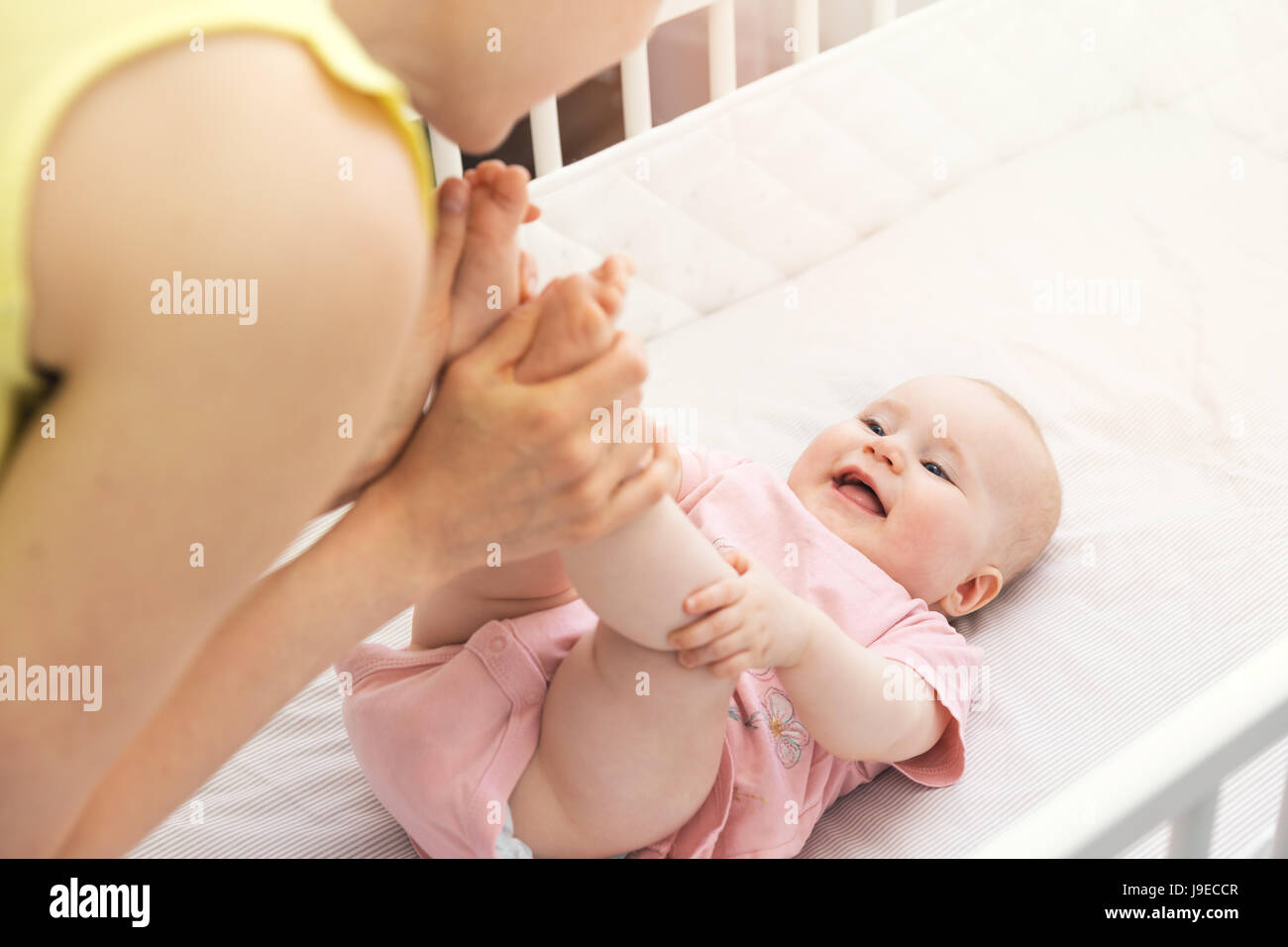 Madre tenere la sua gambe del bambino nel presepe e divertirsi insieme Foto Stock