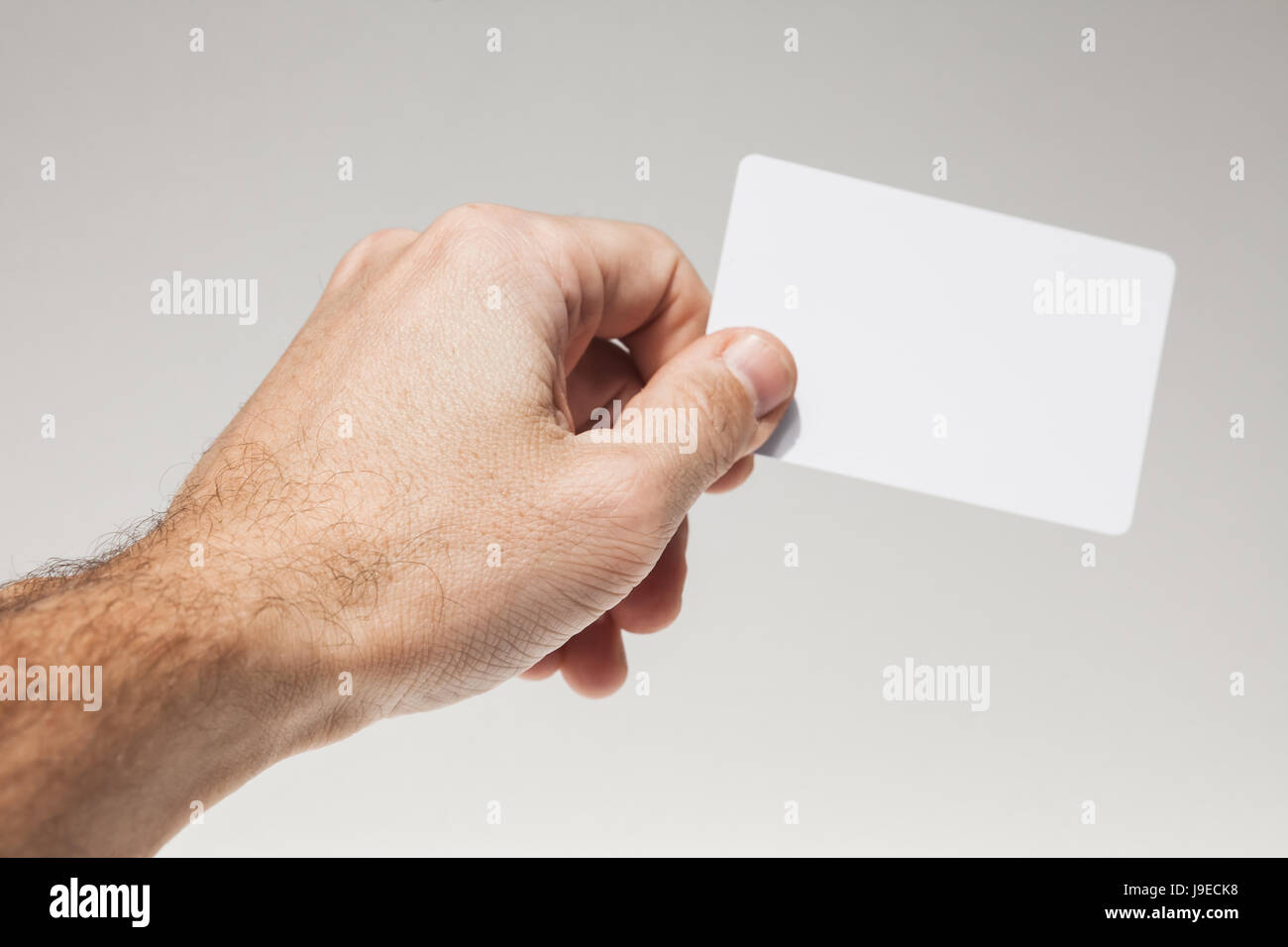 Maschio di mano trattiene bianco scheda vuota su uno sfondo grigio, close up studio foto Foto Stock