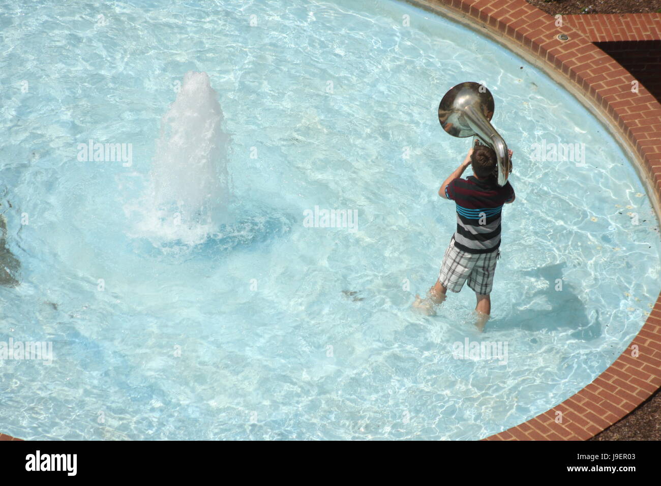 Giovane ragazzo giocando tuba nella fontana di acqua nel giorno di estate Foto Stock