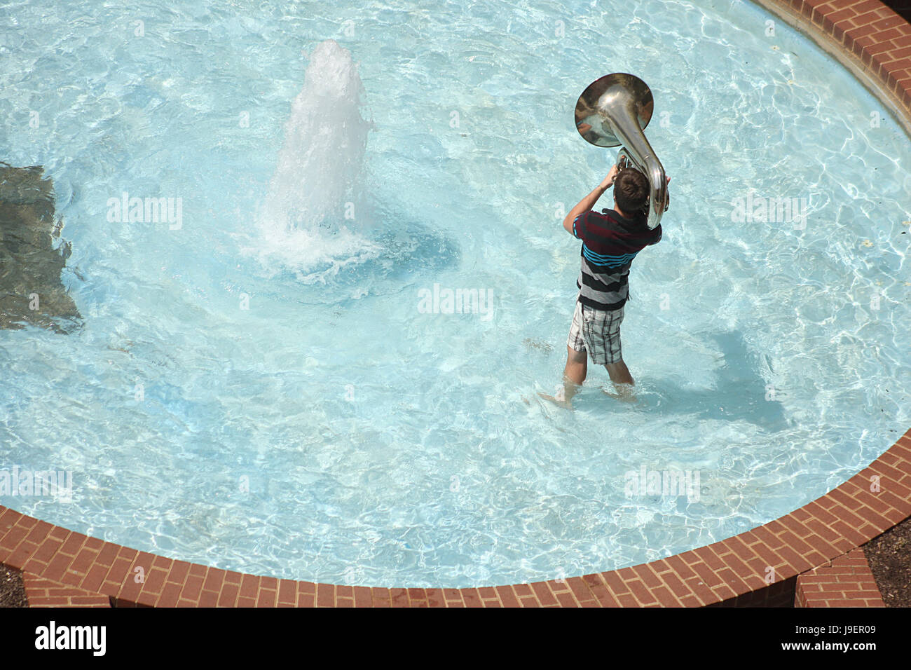 Giovane ragazzo giocando tuba nella fontana di acqua nel giorno di estate Foto Stock