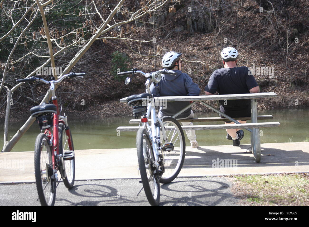 Due uomini adulti in appoggio sul banco dal fiume dopo la corsa in bicicletta Foto Stock