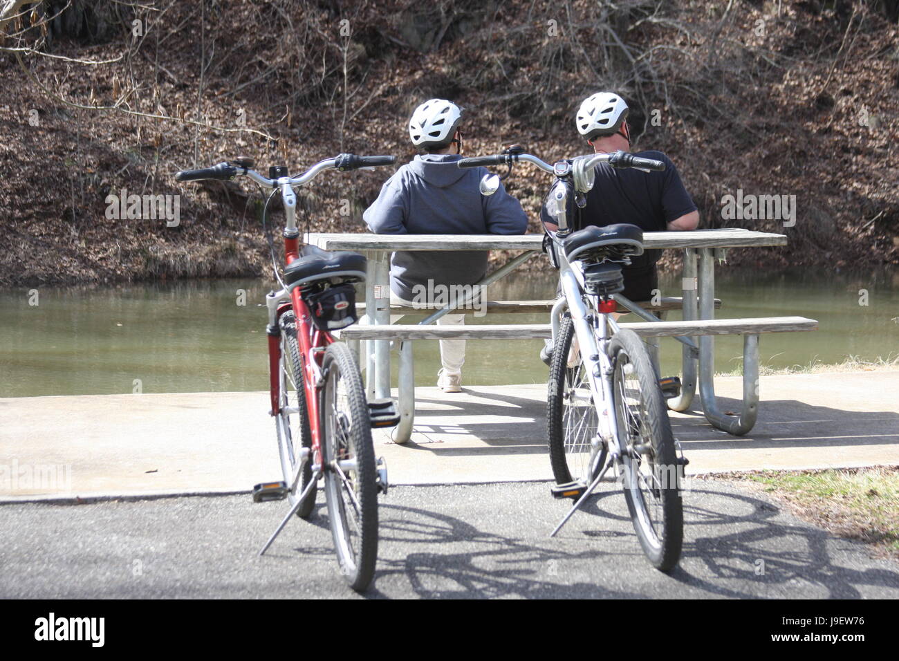 Due uomini adulti in appoggio sul banco dal fiume dopo la corsa in bicicletta Foto Stock