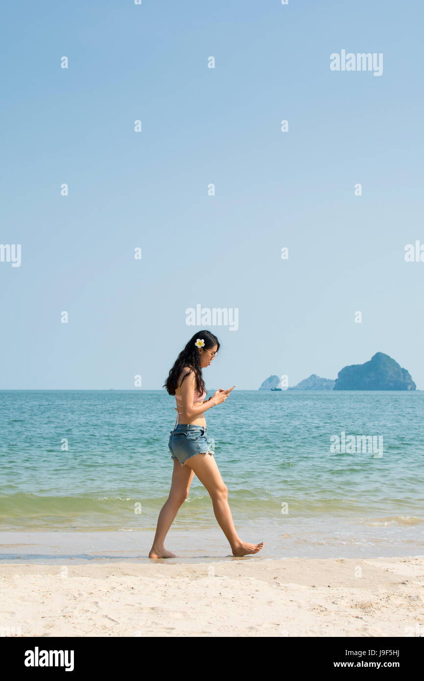 Ragazza guardando smart phone e camminare sulla spiaggia Foto Stock
