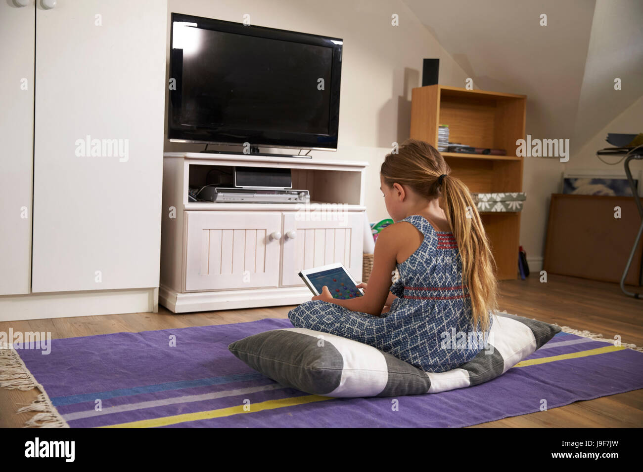 Ragazza guarda la televisione e con tavoletta digitale nella sala giochi Foto Stock