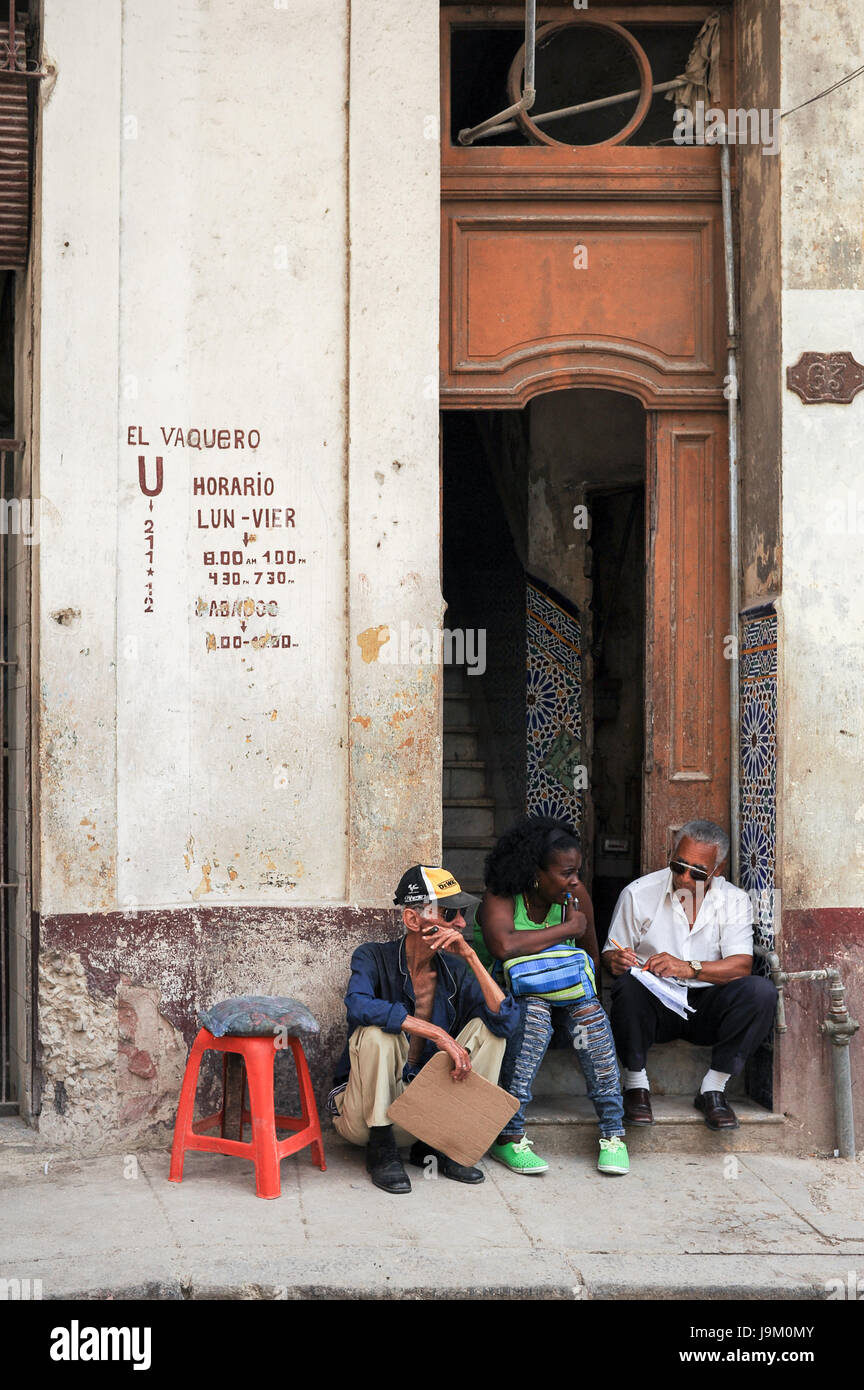 Cubani locali seduti e fumare il sigaro sulla porta di casa a La Habana, Cuba Foto Stock