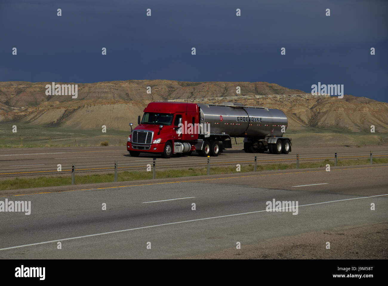 Un Rosso Freightliner Semi-Truck tira un "d'Argento" Groendyke cisterna rimorchio verso il basso un rurale noi Interstate. Foto Stock