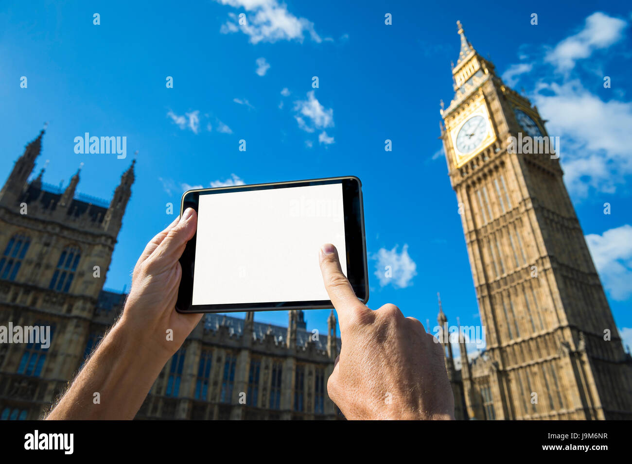 La mano di toccare lo schermo del tablet vuoto di fronte al Big Ben e a Westminster Palace a Londra sotto cieli azzurri Foto Stock