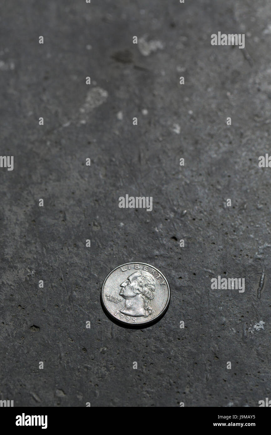 Close-up shot di american 25 centesimi (1998) moneta sul calcestruzzo scuro dello sfondo. La copertina del libro poster o modello con una copia dello spazio. Foto Stock