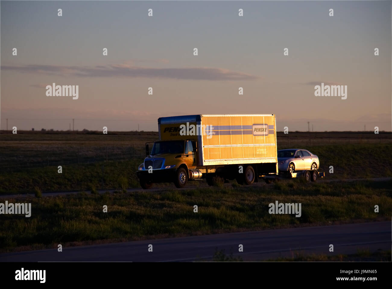 Giallo 'Penske' camion noleggio che viaggia lungo un rurale US Highway durante il traino di una macchina piccola. Foto Stock