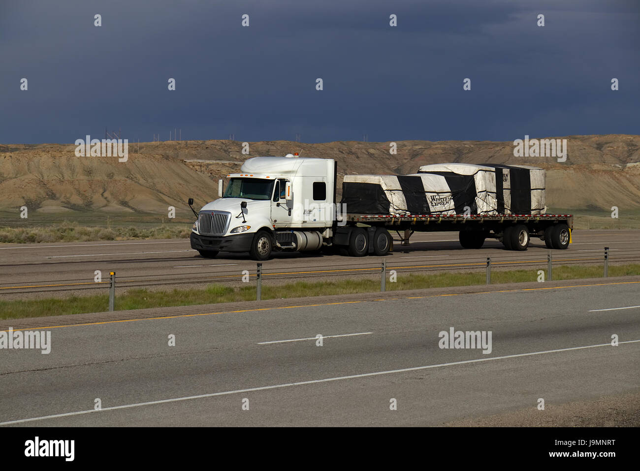 White Semi-Truck trainando un rimorchio dello scanner a superficie piana verso il basso un rurale US Highway. Foto Stock